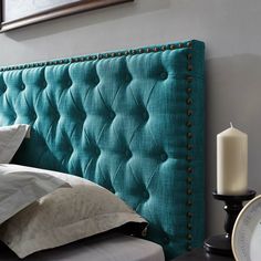 a bed with a blue headboard next to a white plate and candle on a table