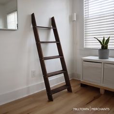 a ladder leaning against the wall next to a potted plant in a white room