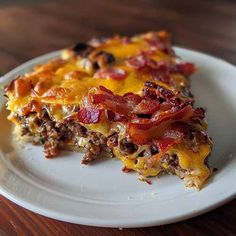 a slice of breakfast casserole on a white plate with bacon, cheese and tomato