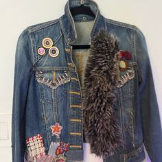 a denim jacket with patches and buttons on it, hanging up against a white wall