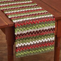 a table runner with red, green and white designs on it sitting on top of a wooden table