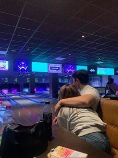 a man and woman sitting at a bowling alley with their arms around each other as they hug