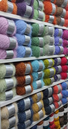 rows of skeins of colored yarn on display in a store with white shelves