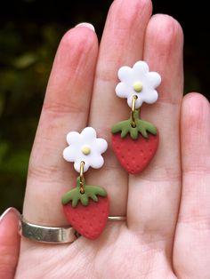 two small strawberry shaped earrings with flowers on them are being held in someone's hand