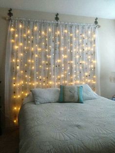 a bed with lights hanging from the headboard and pillows on top of it, in front of a window