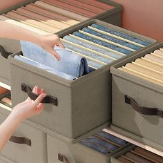 a woman is reaching for some folded clothes in a drawer with two bins on it