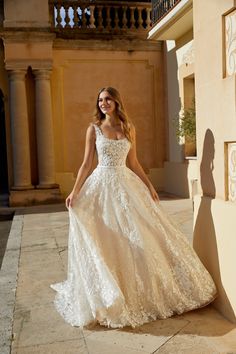 a woman in a white wedding dress standing on the side of a building with her arms behind her back