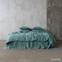 a bed with two pillows on top of it in front of a wall and concrete floor