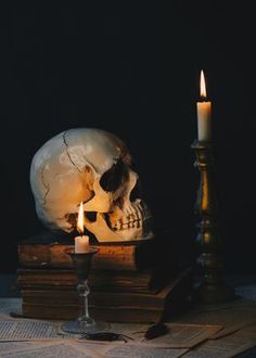 a human skull sitting on top of a pile of books next to a lit candle