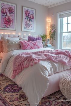 a bed with pink blankets and pillows in a bedroom next to a window filled with lights