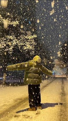 a person standing in the snow with their arms out to catch some snowflakes