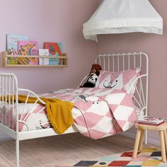 a child's bedroom with pink walls and white metal bed frame, teddy bear on the pillow