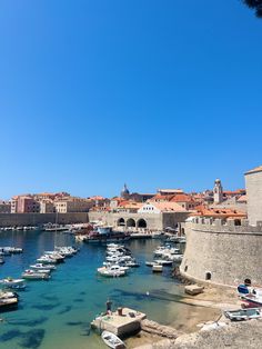 boats are parked in the water near an old city with stone walls and red roofs