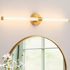 a bathroom light that is next to a vase with flowers in it and a mirror