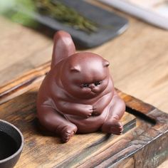 a small brown cat figurine sitting on top of a wooden table next to a black bowl