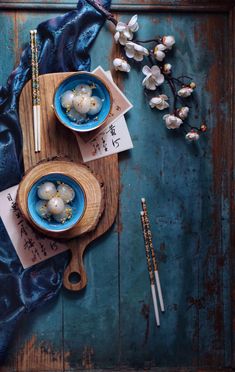 two blue bowls with food and chopsticks on a wooden board next to flowers