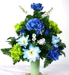 a vase filled with blue and green flowers on top of a white table next to a wooden block