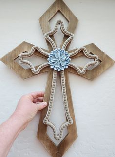 a hand is holding up a wooden cross with blue flowers on the front and sides