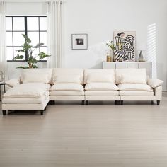 a living room with white furniture and large windows on the wall, along with hardwood flooring