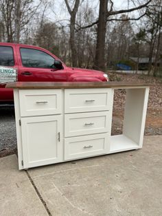 a red truck parked next to a white cabinet on the side of a road in front of some trees