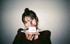 a woman holding a plate with a cake on it in front of her face and looking at the camera