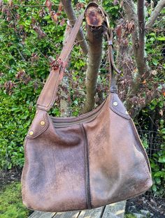 "Fantastic slouch hobo bag from vintage Lucky Brand, bag is brown leather with shoulder strap and zippered closure.  Antiqued brass ring and buckle, with brass grommets at the sides.  Dusty red fabric lining is intact, with zippered internal pocket.  Note that the lining was cut away from the shoulder strap, a great move in my opinion as the leather stays on the shoulder better.  Bag is in good vintage condition, very soft and well loved. Dimensions:   Height 12\" Width 16\" Depth 3\" Strap drop 12\"" Vintage Tote Shoulder Bag With Metal Hardware, Vintage Hobo Bag, Vintage Leather Bags With Hardware Details, Vintage Brown Hobo Bag With Adjustable Strap, Vintage Leather-backed Hobo Satchel Bag, Vintage Leather Bags With Hardware, Travel Tote Hobo Bag With Brass Hardware, Travel Hobo Tote Bag With Brass Hardware, Vintage Brown Hobo Bag With Leather Backing