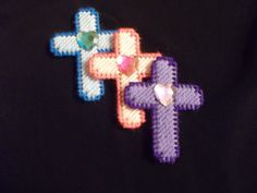 two cross shaped brooches are on a black shirt and one has a pink, purple, and green bead