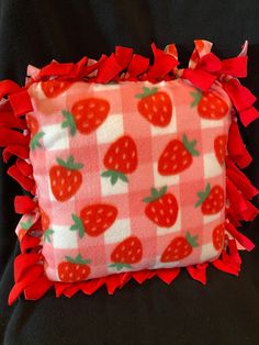 a red and white strawberry print pillow with ruffles on the bottom, sitting on a black surface