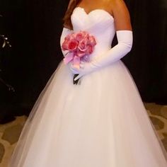 a woman in a white wedding dress holding a pink rose bouquet and wearing long gloves