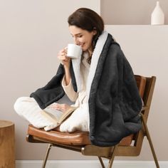 a woman sitting in a chair holding a book and drinking from a mug while reading a book