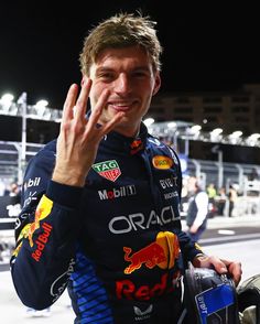 a man with his hand up to his face while standing in front of a race car