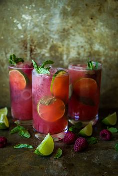 three glasses filled with fruit and garnish sitting on top of a wooden table