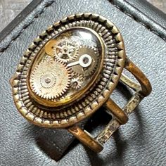 an old watch is sitting on top of a leather case and has gears attached to it