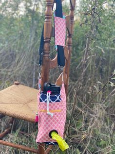 a pink and white bag hanging from a wooden chair in the grass with trees behind it