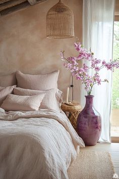 a bedroom with pink flowers in a purple vase on the bed and white linens