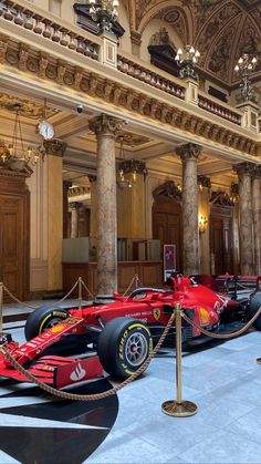 a red race car is on display in a museum with columns and chandeliers