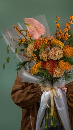 a woman holding a bouquet of flowers in front of her face and wearing a brown jacket