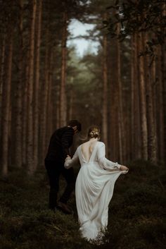 a bride and groom walking through the woods