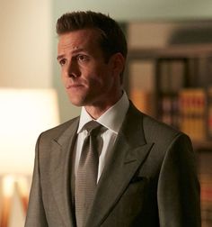 a man wearing a suit and tie standing in front of a bookshelf with a lamp