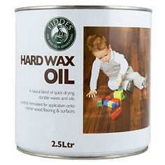 a can of hard wax oil sitting on top of a wooden floor next to a baby playing with blocks