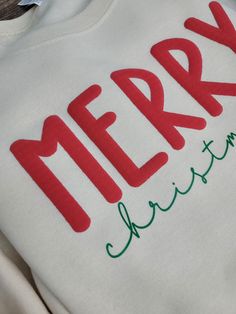 a white sweatshirt with the word merry written in red and green on it's chest