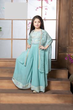 Enhance the elegance of your young one with this stylish and comfortable palazzo set, which includes a shrug, ensuring a stunning appearance on any occasion. Crafted from premium-quality georgette fabric in a serene shade of blue, this ensemble comprises a top, bottom, and shrug. The top is a masterpiece of meticulous artistry, adorned with intricate thread embroidery subtly highlighted by the shimmer of mirrors, which adds a touch of refinement throughout. The palazzo-style bottom, with its fine pleats and secure hook closure, imparts a voluminous and graceful appearance. The hemline of the pants is adorned with thread embroidery that harmoniously matches the top, creating a cohesive and sophisticated look. The shrug, in the same matching hue, is adorned with mirrors scattered throughout, Spring Designer Wear Blue Sets, Designer Spring Blue Set, Blue Palazzo Set For Spring Party, Designer Blue Sharara For Spring, Blue Sharara For Spring, Eid Blue Maxi Length Palazzo Set, Elegant Blue Palazzo Set For Summer, Blue Maxi Length Palazzo Set For Eid, Blue Maxi-length Palazzo Set For Eid