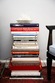 a stack of books sitting on top of a wooden table next to a white chair