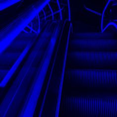 an escalator with blue lighting going down it's side and the bottom