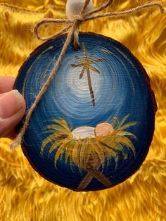 a hand holding a painted ornament with a palm tree on it and a star in the sky