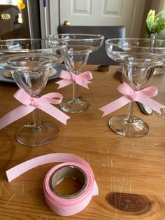 four wine glasses with pink bows on them sitting on a table next to a roll of tape