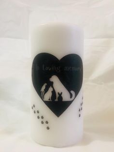 a white candle with a black heart and dog silhouette on the front, surrounded by paw prints