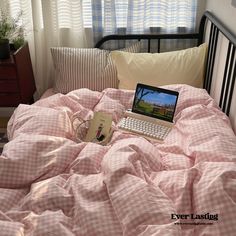 an open laptop computer sitting on top of a pink comforter in a bed room