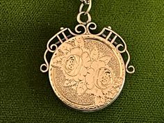 "Description: Beautiful round vintage 10K yellow gold fob locket necklace. This antique fob locket features an etched design of two flowers surrounded by leaves on the front. The background behind the roses is a textured surface. There are etched notches on the outer rim of the rose design all the way round the round locket front. The back side is plain with no etched design. This antique locket has a decorative and ornate scroll openwork frame around the top that goes downward to the mid sectio Victorian Medallion Jewelry With Hallmark, Victorian Hallmark Jewelry For Memorial, Victorian Memorial Jewelry With Hallmark, Victorian Charm Necklace For Formal Occasions, Victorian Formal Necklace With Charms, Victorian Style Formal Necklaces With Charms, Victorian Formal Charms Necklace, Ornate Necklace, Vintage Locket