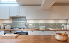 a kitchen with wooden counter tops and white cabinets, along with a bowl of fruit on the counter